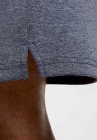 Graues Baumwoll-T-Shirt mit abgerundetem, geteiltem Saum, das eine weiche Textur und ein subtil gemustertes Melange-Design aufweist. Nahaufnahme des Ärmelrands.