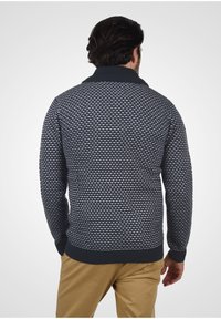 Strikket sweater i marineblå og hvid, med et tekstureret mønster, ribbet krave og manchetter samt en afslappet pasform. Synligt design på bagsiden.