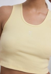 Top court jaune côtelé avec un col arrondi et le texte brodé « self » à l'avant. Design ajusté avec une texture douce.