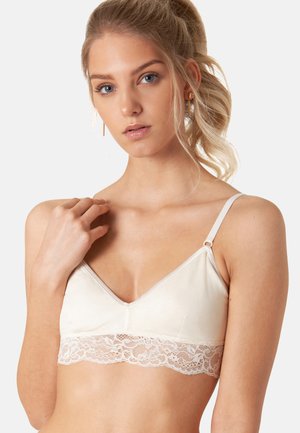 Bralette beige chiaro realizzato in tessuto morbido, con bordo in pizzo lungo il fondo, spalline regolabili e design a scollo a V.