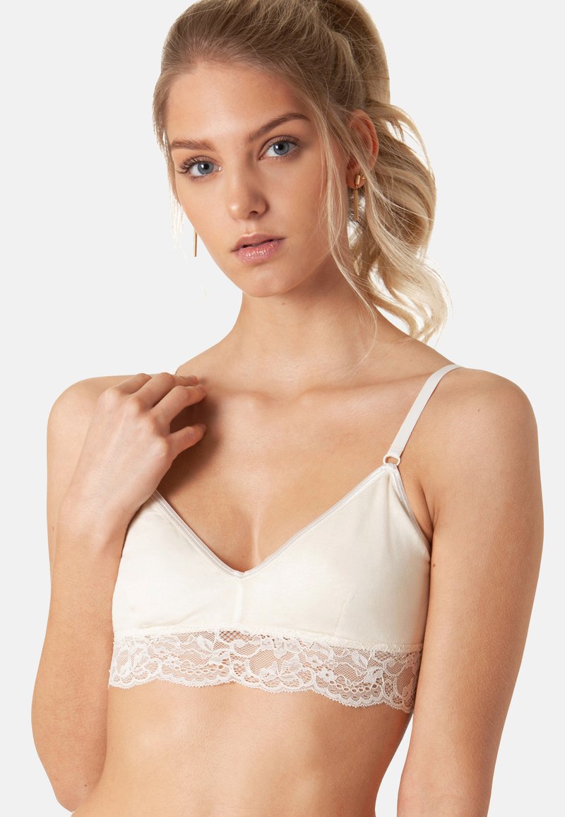 Bralette beige chiaro realizzato in tessuto morbido, con bordo in pizzo lungo il fondo, spalline regolabili e design a scollo a V.