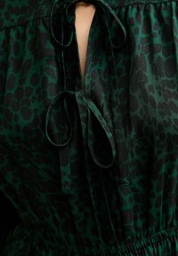 Groene en zwarte luipaardprint blouse, met een striksluiting bij de halslijn en een elastische taille voor een aansluitende pasvorm. Glad stoftextuur.