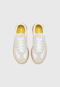 Svijetlosivi i bijeli atletski tenisice s gumenenom potplatom, s tri sive pruge, vezicama i žutom unutrašnjom površinom s "adidas" markom.