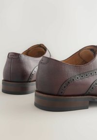 Chaussures en cuir marron avec une finition texturée et des perforations décoratives. Semelles robustes avec un design en couches et des couleurs contrastées.