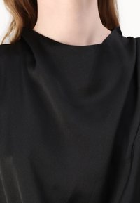 Top in tessuto nero e liscio con colletto alto e design drappeggiato, che presenta una leggera lucentezza e una consistenza morbida.