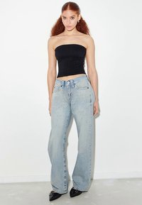 Svart stroppeløs topp med teksturert design; lyseblå vidbukser med naglede detaljer; svarte spisse sko. Minimalistisk bakgrunn.