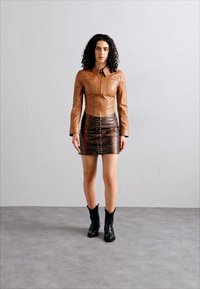 Jachetă din piele maro cu fermoar, asortată cu o fustă mini din piele de șarpe maro și cizme cowboy negre. Texturi netede cu modele distincte.