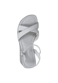 Vit sandal med korsremdesign, texturerad mellansula, justerbar vristrem och en subtil metallisk accent längs kanten.