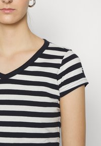 Pruhované tričko s námořnickými a bílými horizontálními pruhy, krátkým rukávem a designem ve tvaru V. Vyrobeno z měkké bavlny s jemnou texturou.