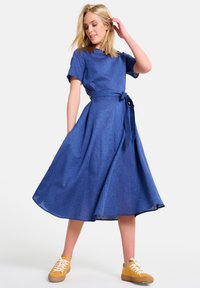 Denim sinine kleit lühikeste varrukatega, õhku tõstetud vöökoha ja laieneva seelikuga. Includes sobivast kangast vöö. Koos heledate tennekingadega.