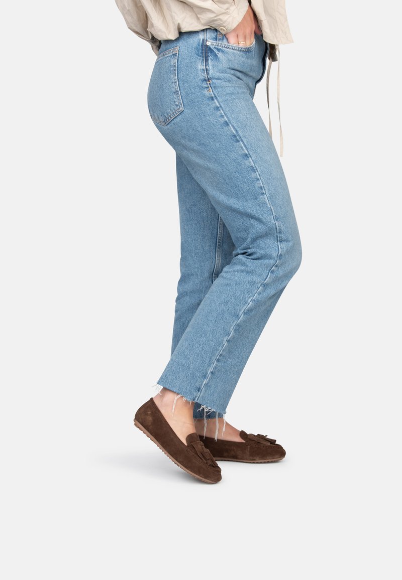 Brown suede moccasin shoes with a decorative fringe, worn with light blue distressed straight-leg jeans featuring frayed hems.