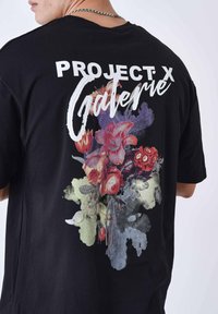 Zwarte katoenen t-shirt met een grote bloemgrafiek op de rug in levendige kleuren, voorzien van de witte tekst "PROJECT X Galerie."