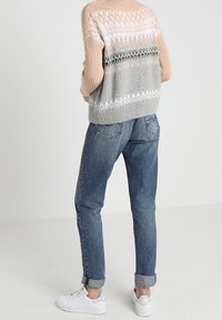 Maglione lavorato a maglia in tonalità pastello con un motivo geometrico, abbinato a jeans in denim azzurro chiaro arrotolati e sneaker bianche.