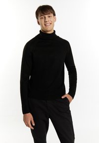 Schwarzer Rollkragenpullover aus gestricktem Stoff, mit langen Ärmeln, gerippten Bündchen und einem lockeren Schnitt. Tragen mit dunklen Hosen.