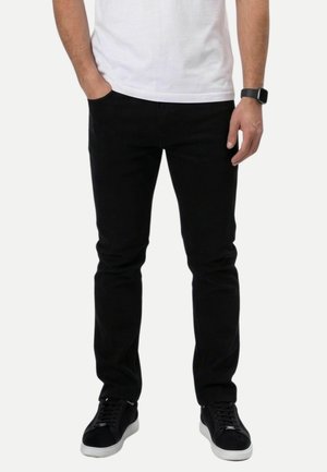 Homme portant un pantalon slim noir, des baskets noires avec semelles blanches, un t-shirt blanc et une montre connectée noire au poignet gauche.