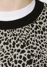 Acercamiento a un suéter de estampado de leopardo con un cuello de canalé negro, llevado sobre una camiseta blanca de cuello redondo.