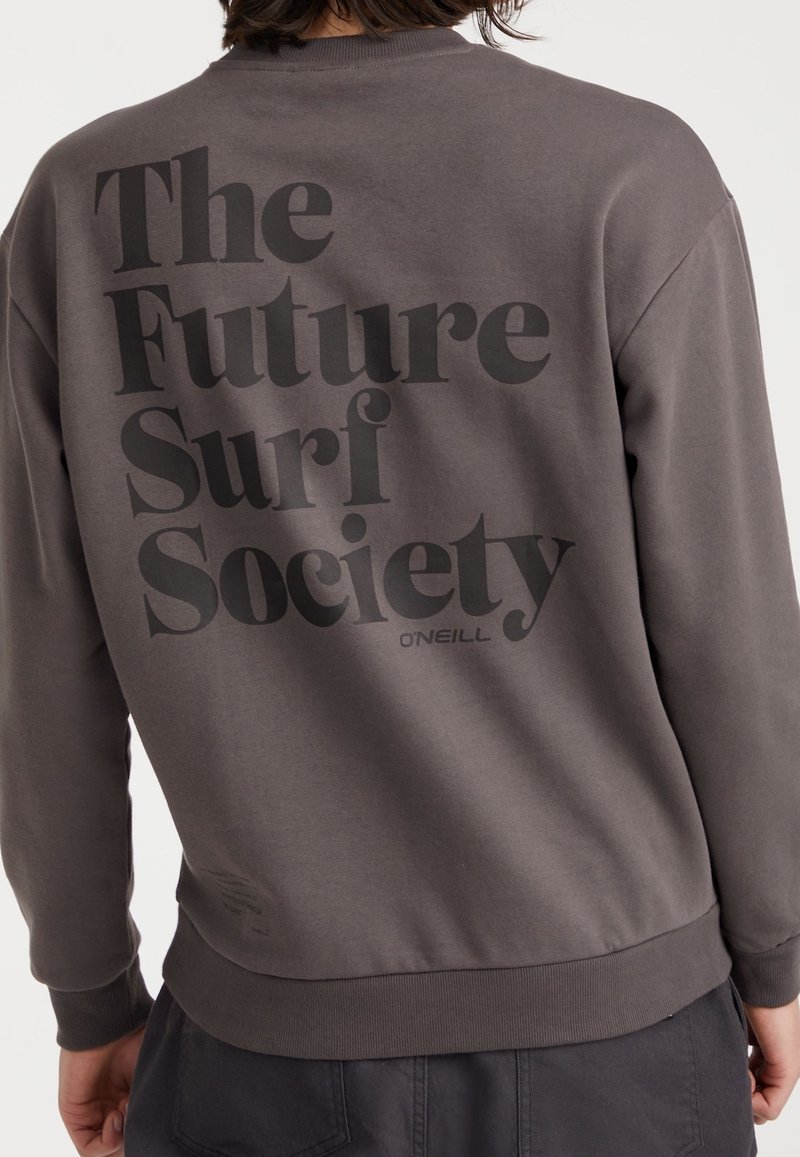 Personne portant un sweat-shirt marron avec un grand texte noir dans le dos indiquant "The Future Surf Society" et un petit logo "O'Neill".