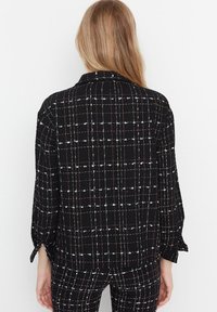 Blazer a quadri neri con accenti bianchi e rossi, dotato di colletto, maniche lunghe e vestibilità rilassata. Tessuto testurizzato con motivo a reticolo.