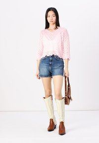Rausvų siūlų viršus su V formos iškirpte, derinamas su džinsiniais šortais ir kreminės spalvos iki kelių aukštakulniais cowboy botais su rudi akcentais. Modelis laiko rudą rankinę.
