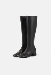 Bottes en cuir noires jusqu'aux genoux avec une texture lisse, un bout carré et un talon épais. Présente une fermeture éclair latérale visible pour un enfilage facile.