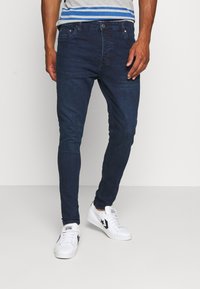 Mörkblå slim-fit jeans i denim; har en klassisk fem-fickorsdesign och kompletteras av vita sneakers.