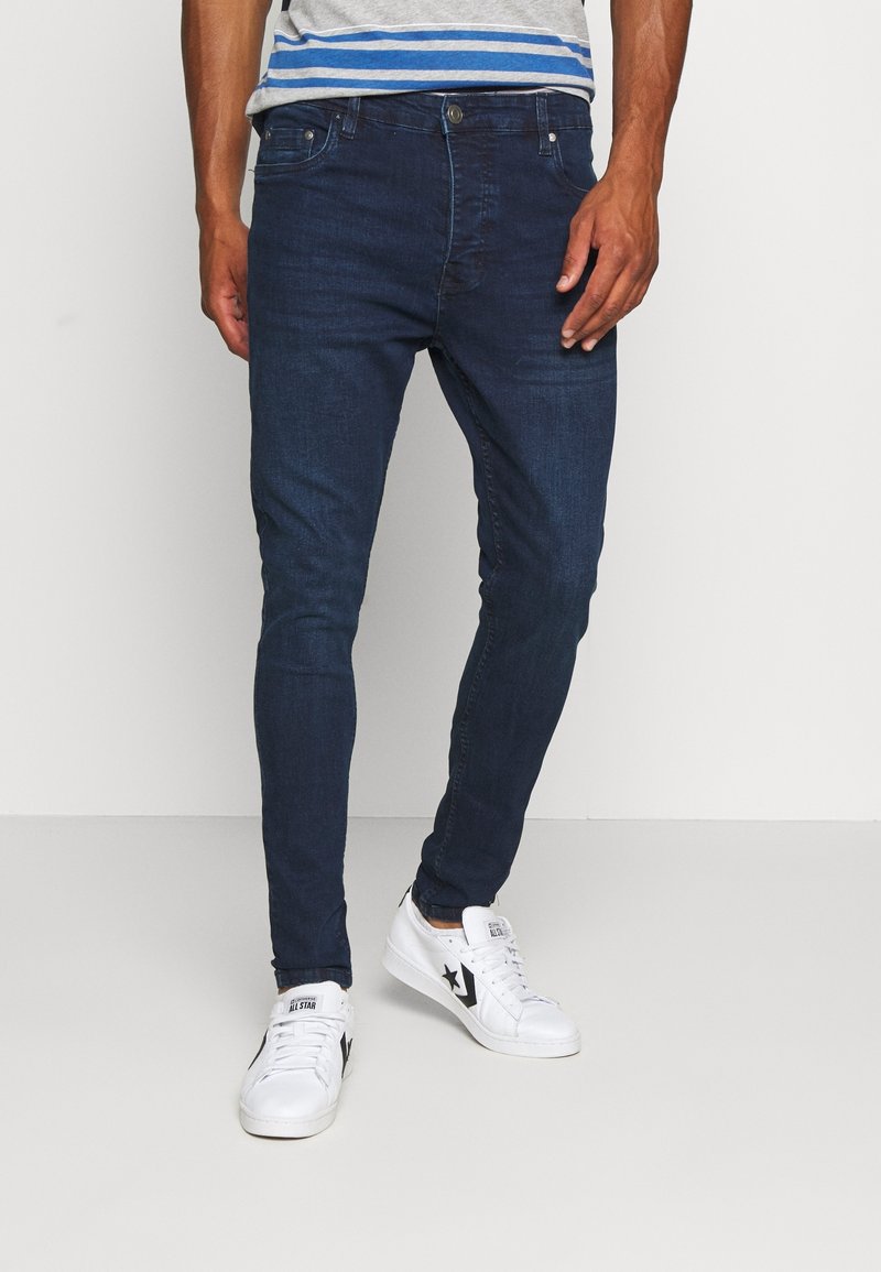 Mörkblå slim-fit jeans i denim; har en klassisk fem-fickorsdesign och kompletteras av vita sneakers.