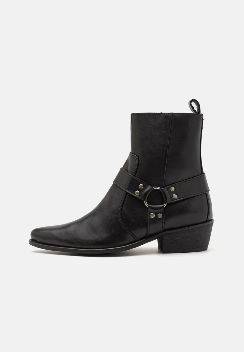 Schwarze Leder-Stiefeletten mit spitzer Zehenform, seitlichem Riemen mit runder Hardware-Akzentuierung und niedrigem Blockabsatz. Glatte Textur.