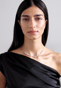 Collana d'argento con piccoli gemme trasparenti, indossata su un top nero scollato. Texture liscia e design delicato.