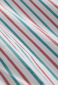 Baumwollstoff mit schmalen roten und türkisfarbenen Streifen auf weißem Hintergrund; glatte Textur, zerknittertes Aussehen.