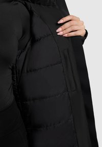 Sort isoleret jakke med en glat overflade og quiltet inderside. Har en sidelomme og et slankt, minimalistisk design.