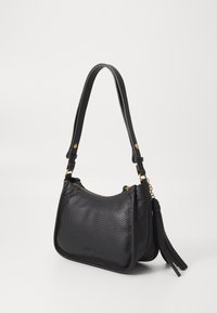 Bolso de hombro de cuero negro con textura de grano, accesorios de hardware dorado, un borlón decorativo y una forma curva. Incluye una correa ajustable.
