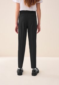 Black tailored trousers with a fitted waistband, featuring two rear pockets and a straight-leg cut. Worn with black patent shoes.