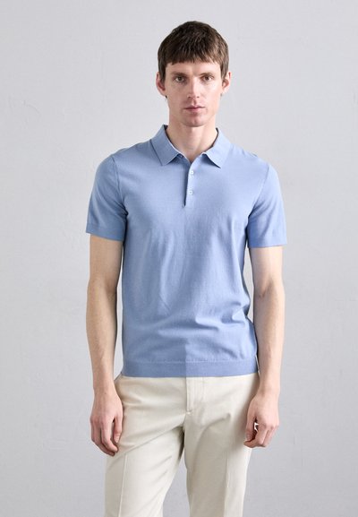Lys blå kortærmet polo-shirt med klassisk krave og tre-knaps lukning. Blødt stof og figurbetonet design. Matchet med cremefarvede bukser.