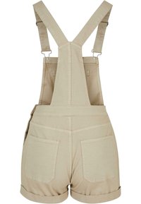 Salopette courte beige en coton avec revers roulés, deux poches à l’arrière, et bretelles croisées réglables avec attaches métalliques.