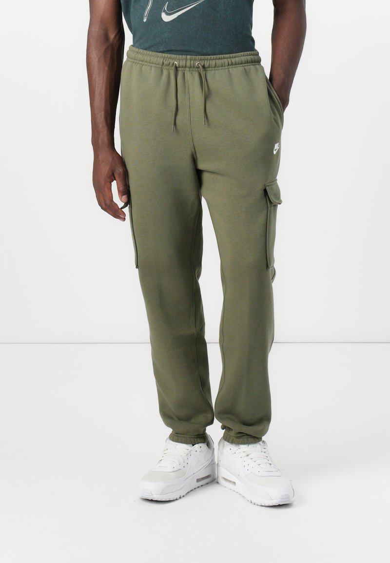 Olive-green sweatpants with elastic waistband, side cargo pockets, tapered ankles, and subtle Nike logo embroidered on left leg.