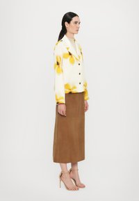 White jacket with yellow floral print, black buttons; brown suede midi skirt; beige strappy heeled sandals; smooth, structured fabric.