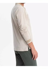 Polo à manches longues beige clair avec col, en tissu texturé, poignets contrastants avec rayures et fentes latérales pour plus de confort.