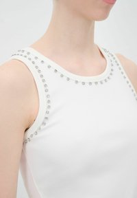 Top bianco senza maniche con scollatura rotonda, decorato con strass argentati lungo i bordi, realizzato in tessuto morbido e elastico.
