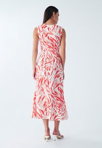 Garais kleita ar baltu pamatni un sarkaniem abstraktiem viļņveida rakstiem, bezroku dizains un plūstoša siluets, demonstrējot gludu auduma tekstūru.