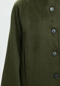 Groene wollen jas met een ronde kraag, sluiting met knopen aan de voorkant, zijzakken en een textiele stof met een gladde afwerking.
