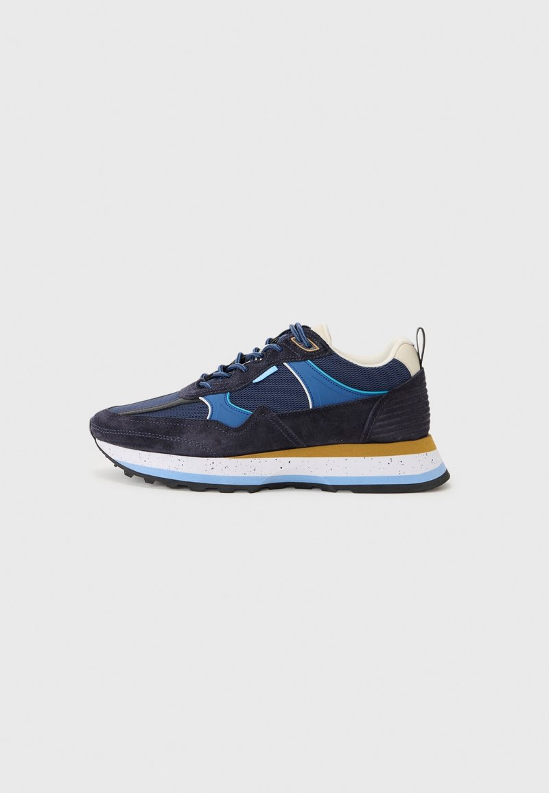 Baskets bleu foncé et noir avec des accents bleus, semelle blanche tachetée jaune et semelle noire, vues de profil sur fond blanc.