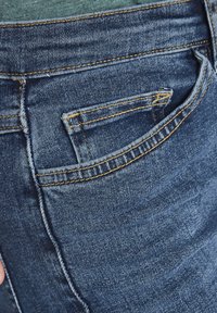 Primo piano della tasca dei jeans di denim blu con cuciture visibili e una piccola tasca per monete all'interno della tasca posteriore più grande.