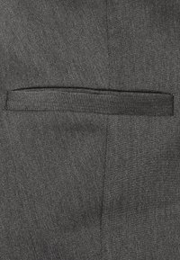 Grijze stof met een subtiel visgraatpatroon. Heeft een platte zak met een nette, op maat gemaakte naad. Geretoucheerd oppervlak, minimalistisch ontwerp.