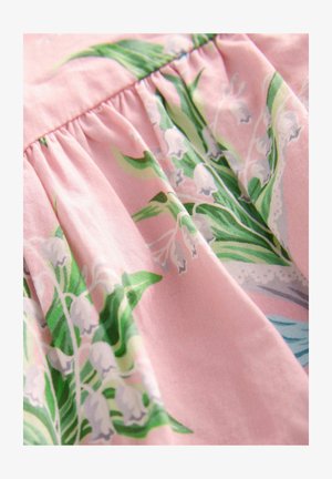 Ziedu audums ar zaļām lapām un baltām ziediem uz maiga rozā fona, ar krokām, kas veido teksturētu izskatu.