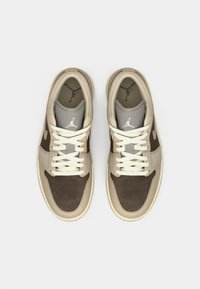 Καφέ και μπεζ αθλητικά παπούτσια με λείο και σουέτ υφή, που διαθέτουν λευκά κορδόνια, γκρι γλώσσα και μαύρο λογότυπο στη φτέρνα και στην εσωτερική σόλα.