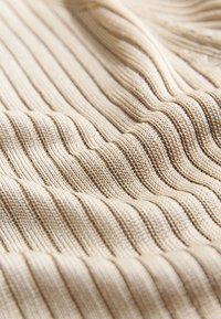 Tissu tricoté côtelé beige avec des rayures texturées verticales créant des plis doux et des ombres sur la surface.