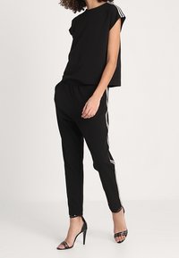 Svart kortärmad crop-top i svart, kombinerad med svarta tapered-byxor med vita sidostråk. Bärs med svarta klacksandaler.