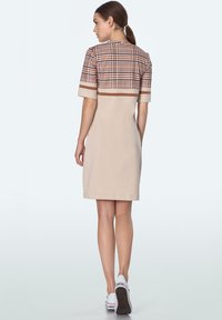 Beżowa sukienka z kratkowanym górnym odcinkiem, krótkimi rękawami i poziomymi brązowymi paskami. Gładka tekstura i dopasowany krój. Prosty design z tyłu.