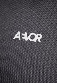 Schwarzes Textilmaterial mit einer strukturierten Oberfläche und einem auffälligen weißen Logo, das "A=VOR" liest. Einfaches, modernes Design.