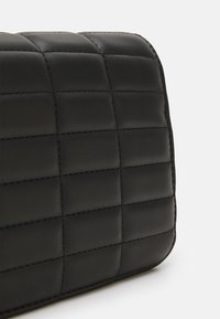 Bolso de mano acolchado negro con un acabado de cuero suave, que presenta rectángulos estructurados y detalles de costura en contraste.